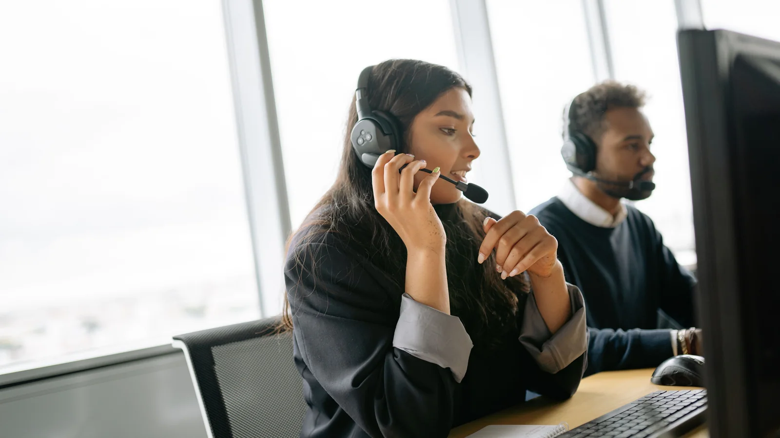Customer service colleagues wearing headsets and working at computers in a bright shared office.