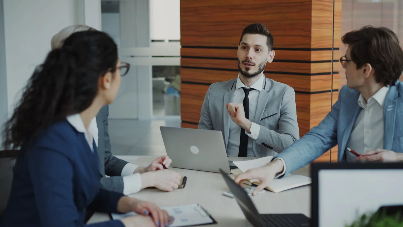 Sales colleagues discussing an enquiry around a table with laptops and notebooks in an office.