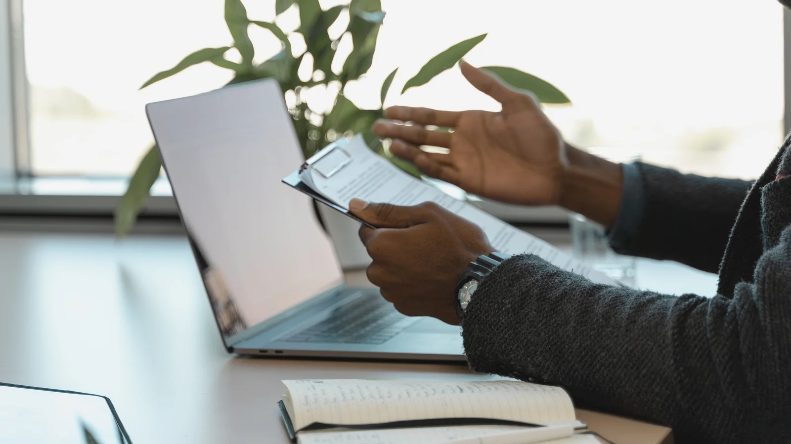 A sales professional reviewing documents beside a laptop and notebook at an office desk.